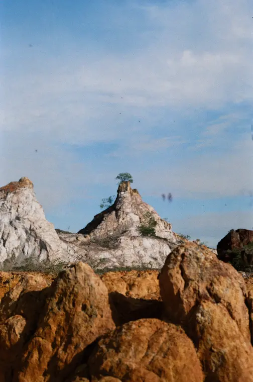 Pale rock spire against a blue sky, orange boulders below, vertical film frame