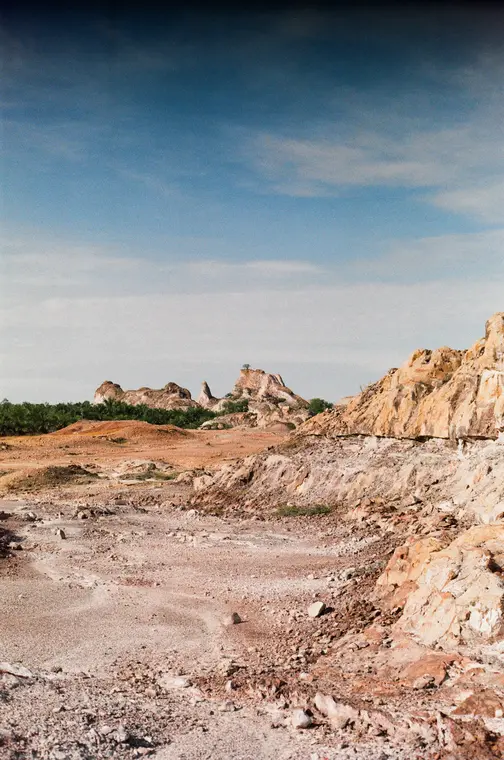 Orange cliff face falling to a dusty trail under a deep blue sky